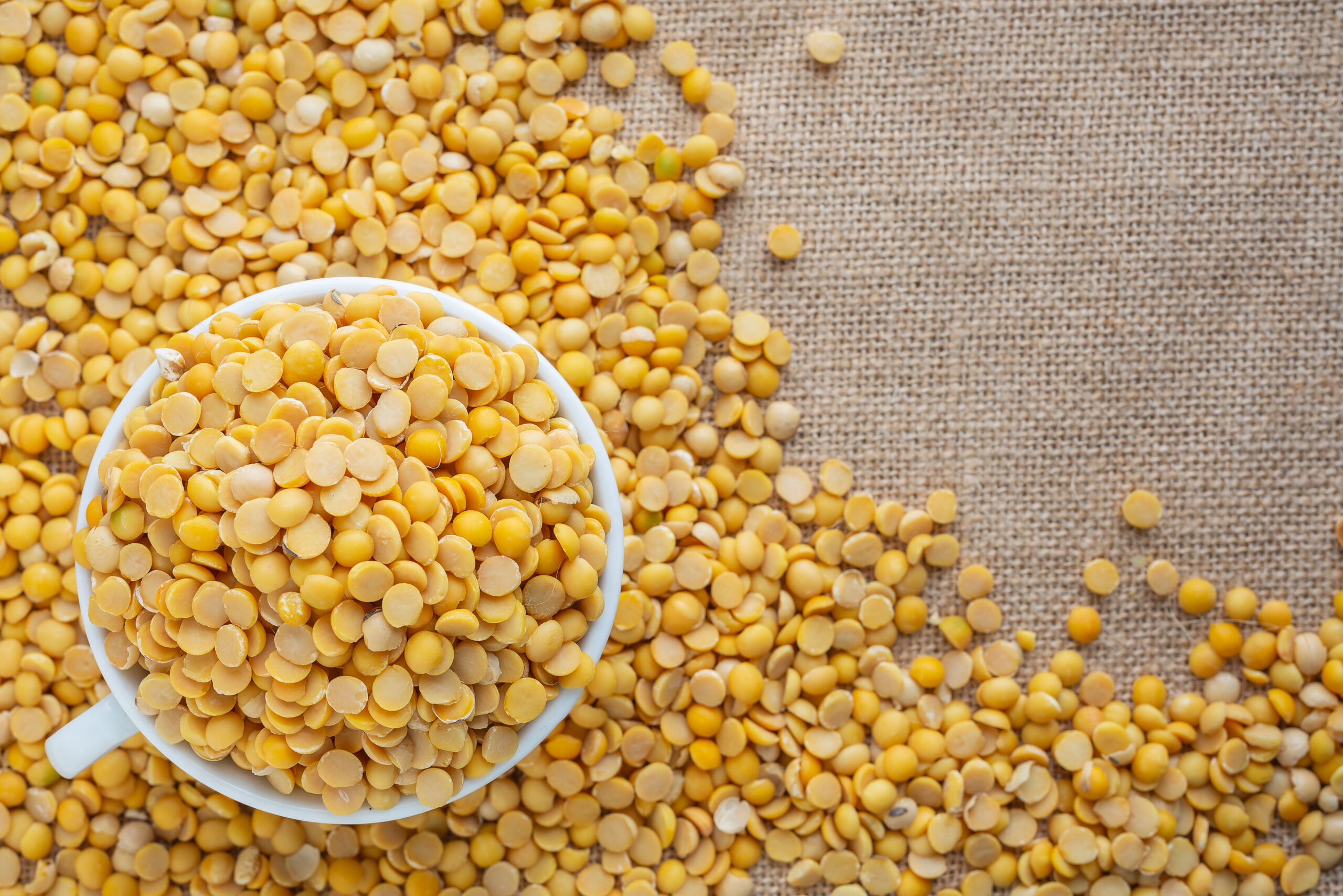 Raw soybeans in a white glass placed on a floor.